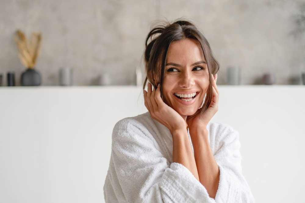 Frau mit gesunder und strahlender Haut, die glücklich in einem Bademantel lächelt, ideal, um die Vorteile der Hautpflege mit Produkten wie Aloe Vera zu veranschaulichen.